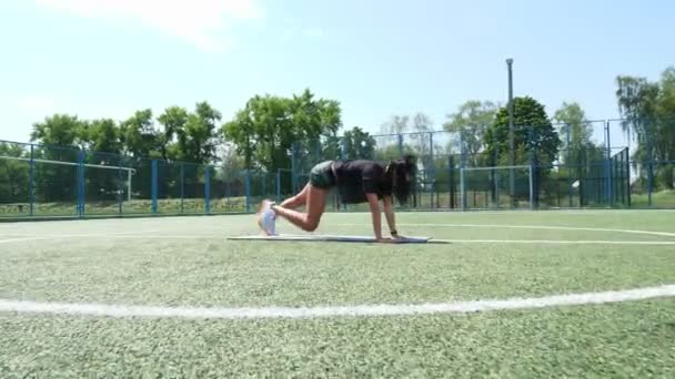 Femme de fitness en vêtements de sport faisant divers exercices sur tapis de sport, sur le terrain de football vert avec des marques blanches, au stade. Sports de plein air. formation en ligne. chaude journée d'été. concept de mode de vie sain — Video