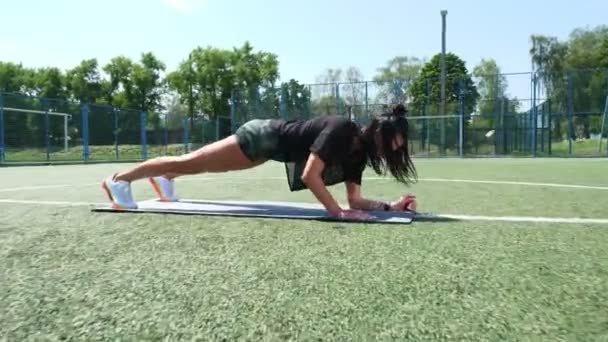 Fitness woman in sportswear doing various exercises on sports mat, on green football field with white markings, at stadium. Outdoor sports. online training. hot summer day. healthy lifestyle concept — Stock Video