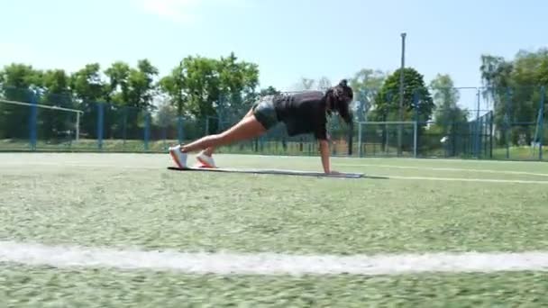 Femme de fitness en vêtements de sport faisant divers exercices sur tapis de sport, sur le terrain de football vert avec des marques blanches, au stade. Sports de plein air. formation en ligne. chaude journée d'été. concept de mode de vie sain — Video