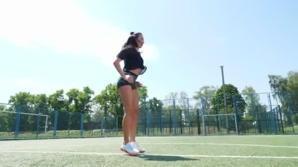 Fitness žena ve sportovním oblečení dělá různá cvičení na sportovní podložce, na zelené fotbalové hřiště s bílými značkami, na stadionu. Venkovní sporty. online školení. Horký letní den. koncepce zdravého životního stylu — Stock video