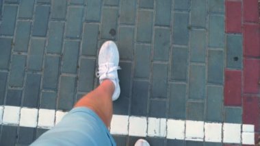 Yakın çekim, üst manzara. Beyaz spor ayakkabılı erkek bacakları beyaz çizgiyi geçiyor ve yere çizilmiş 600 numaraya gidiyor..