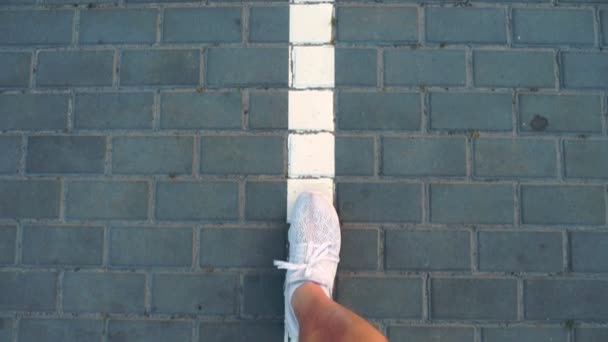 Primer plano, vista superior. piernas masculinas en zapatillas blancas van a lo largo de la línea blanca de marcas de carretera . — Vídeos de Stock