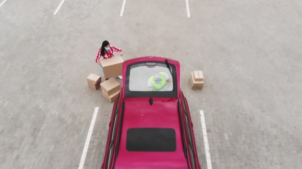 Aero. Top view. Couriers, man and woman, in protective masks and medical gloves shipp cargo and load parcels, boxes of essential goods to car trunk. Delivery service under quarantine, coronavirus — Stock Video