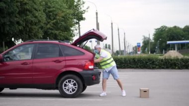 Erkek kurye, özel bir yelek, koruyucu maske, eldivenler, paketleri boşaltma, araba bagajından karton kutular, kargo teslimat servisi karantina altında, koronavirüs salgını.