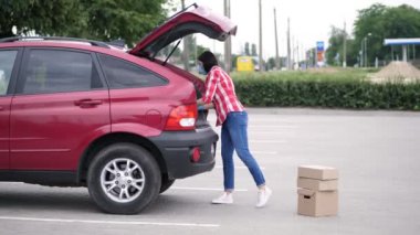 Kadın kurye, özel bir yelek, koruyucu maske, eldivenler, boşaltma paketleri, araba bagajından karton kutular, kargo teslimat servisi karantina altında, koronavirüs salgını.