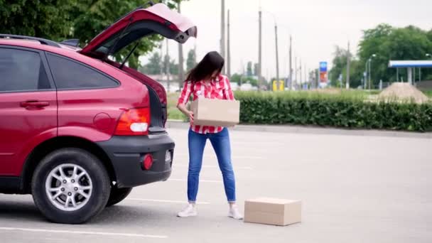 Coursier féminin, en chemise à carreaux rouges et en jeans, déchargeant des colis, des boîtes en carton du coffre de la voiture, à l'extérieur. Service de livraison de fret. — Video