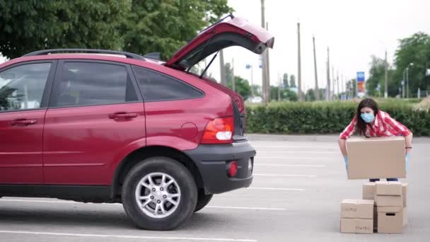 Correio feminino, em máscara protetora, luvas, pacotes de carregamento, colocando caixas de papelão no porta-malas do carro, serviço de entrega de carga em quarentena, surto de coronavírus . — Vídeo de Stock