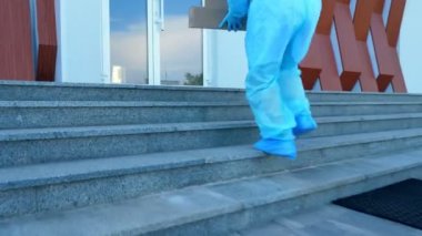 Coronavirüs salgını sırasında hastaneye tıbbi ekipmanla birlikte paket teslimatı. Kurye, koruyucu kıyafetli, doktorun götürmesi için giriş kapısına birkaç kutu bırakıyor..