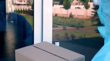 Yakın plan, Coronavirus salgını sırasında hastaneye tıbbi ekipman ya da uyuşturucu taşıyan paket teslimatı. Kurye, koruyucu kıyafetli, hemşireye karton kutular veriyor. Yük taşıma hizmeti sırasında