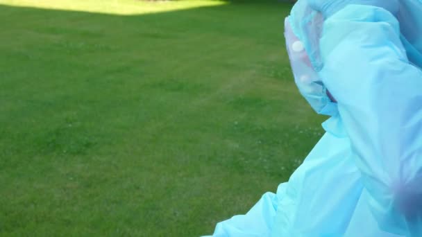 Измученный и уставший врач или медсестра снимают коронавирусную защитную форму, маску, очки. На открытом воздухе, во дворе больницы или медицинского учреждения. Пандемия ковида-19 — стоковое видео