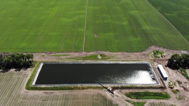 Flygande. Ovanifrån. konstgjord specialbassäng, vattenmagasin, tank eller reservoar för bevattning av jordbruksmark. i närheten finns en pumpstation för vattenintag. Modern teknik inom jordbruket. — Stockvideo