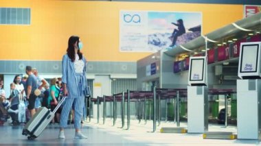 BORISPYL, UKRAINE, 31 Temmuz 2020: tıbbi maskeli, bavullu bir kadın havaalanı terminalindeki boş gişelerin önünden geçer. Coronavirüs salgınından sonra uçuşlar başlıyor..