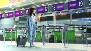 BORISPYL, UKRAINE, 31 Temmuz 2020: tıbbi maskeli, bavullu bir kadın havaalanı terminalindeki boş gişelerin önünden geçer. Coronavirüs salgınından sonra uçuşlar başlıyor..