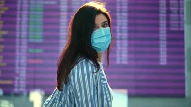 Havaalanında tıbbi maske takan kadın portresi. Uçak yolcusu ve turist kalkış zamanı çizelgesine karşı duruyor. Coronavirüs salgınından sonra hava yolculuğu açılıyor. — Stok video