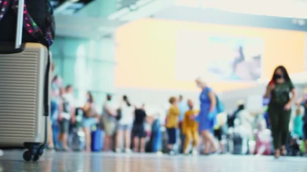 Primo piano di gambe che camminano in scarpe da ginnastica, con valigia su ruote, attraverso la hall dell'aeroporto, sullo sfondo della folla di passeggeri aerei. apertura dei viaggi aerei dopo l'epidemia di coronavirus. — Video Stock