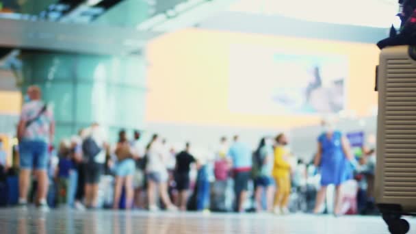Gros plan des jambes en baskets, avec valise sur roues, dans le hall de l'aéroport, sur fond de foule de passagers aériens. ouverture du voyage aérien après l'épidémie de coronavirus. — Video