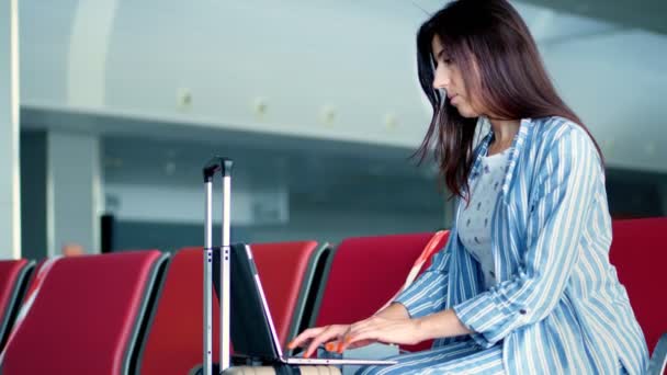 Freelancer, kadın havaalanı terminalinde binmeyi beklerken bilgisayarını kullanarak uzaktan çalışıyor. İş ve seyahat konsepti. Modern uzak iş kavramı. — Stok video