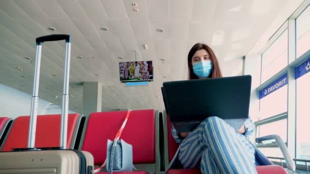 BORISPYL, UKRAINE, 31 juli 2020: kvinna i skyddsmask, med bagage, arbetar på laptop på flygplatsen, i väntan på ombordstigning. Luftledningar som öppnas efter coronavirusepidemin — Stockvideo