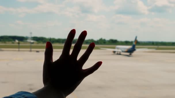 Zblízka, ženy ruku na okenní sklo, na pozadí přistávací dráhy a odlétající letadlo, na letišti. odjezd na letiště — Stock video