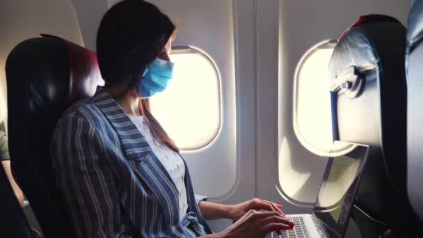 In der Kabine eines Flugzeugs, junge Frau mit Schutzmaske, freie Mitarbeiterin arbeitet am Laptop. Arbeits- und Reisekonzept. Flüge nach Coronavirus-Epidemie eröffnet — Stockvideo