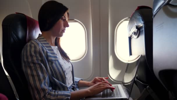 Jeune femme, pigiste travaille, en utilisant un ordinateur portable tout en voyageant en avion. assis près de la fenêtre dans l'avion. concept travail et voyage. — Video