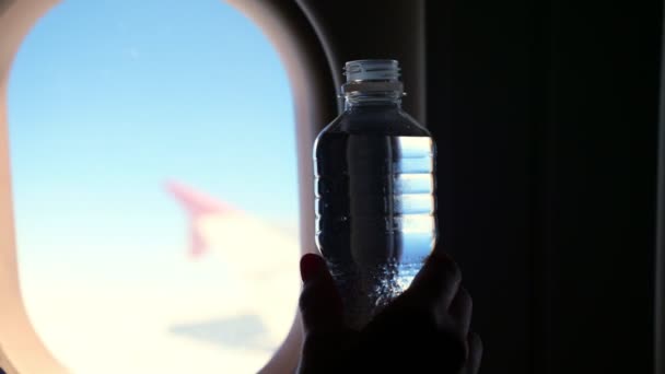 Närbild, mörk siluett av kvinna öppnar liten plast vattenflaska, dricker vatten mot bakgrund av ett flygplan belysning. — Stockvideo