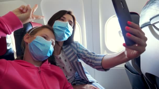 Mujer con niño, en máscaras protectoras, comunicándose en videollamada a través de un dispositivo inteligente. tomar video o hacer selfie, mientras está sentado dentro del avión. vuelos abiertos después de la epidemia de coronavirus. — Vídeos de Stock