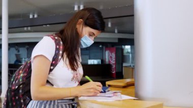 Koruyucu maskeli bir kadın, elinde pasaport ve biletler var, belgeleri dolduruyor, havaalanında tıbbi anket dolduruyor. Coronavirüs salgınından sonra yeni kurallar ve kısıtlamalar. Uçuşların devamı