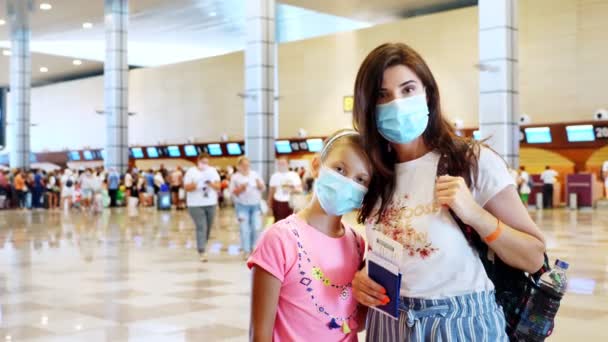 Kvinna och flicka barn i masker på flygplatsen, mot bakgrund av incheckningsdiskar och flygpassagerare med bagage. flygningar som återupptas efter utbrottet av coronavirus. Öppnar gränser. resor öppna. — Stockvideo
