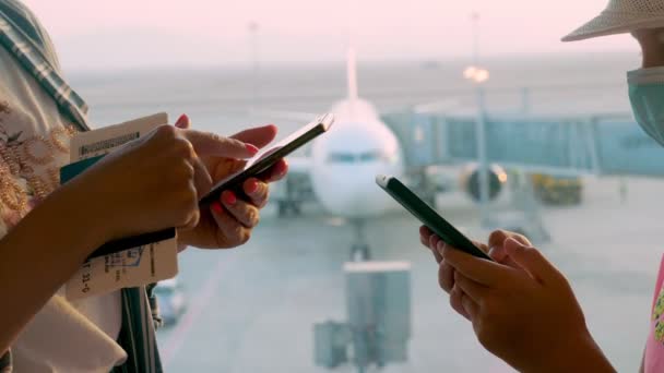 拍手叫好。持护照和罚单的妇女和少女在机场使用手机，在全景窗口前展示跑道和大飞机景观。在验尸报告后重新开放的航班 — 图库视频影像