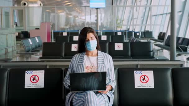 Femme, en masque de protection, utilise un ordinateur portable, assis dans le salon vide de l'aéroport, attendant de monter à bord d'un vol. les voyages aériens ont rouvert après la fin de l'éclosion de coronavirus. Ouverture des frontières. Voyage ouvert. — Video