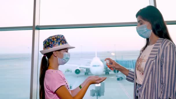 Kvinna i mask, strör en antiseptisk på barnen händer, framför panoramafönster med landningsbana och stora plan utsikt, på flygplatsen. flygningar som återupptas efter utbrottet av coronavirus. Öppnande av gränser — Stockvideo