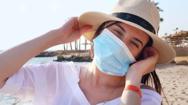 Portrét ženy ve slunečním klobouku, která si sundá ochrannou masku, na mořském pozadí, pláž s palmami. slunečný teplý den. konec sebedestrukce Covid-19 — Stock video