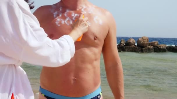 Zbliżenie, nakładanie kremu przeciwsłonecznego lub spray balsam na skórę człowieka. na plaży, w gorącym słońcu, na tle morza. Ochrona przed słońcem i promieniowaniem UV. ochrona skóry — Wideo stockowe