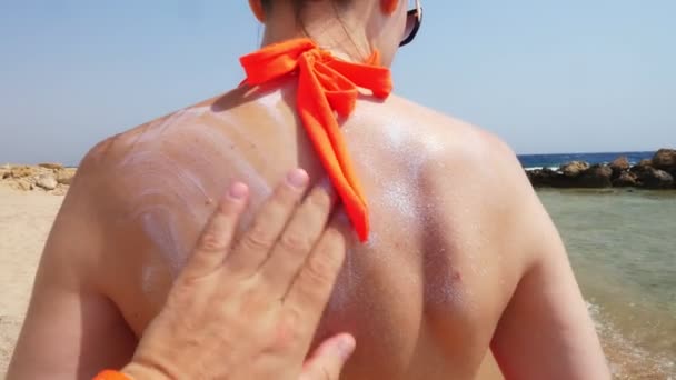 Close-up, male hand applies sunscreen or spray lotion to skin of female back. on the beach under the hot sun, against the backdrop of the sea. Sun and UV protection. skin protection — Stock Video