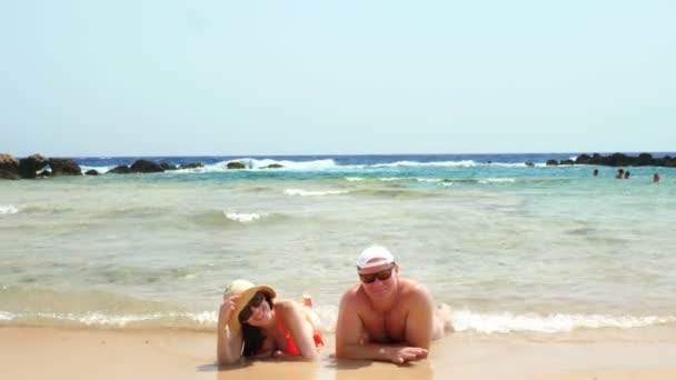 Paar verliefd, mooie jonge vrouw en man met zonnebril en zonnehoed, liggen op het zandstrand, genietend van warm zeewater en zonnestralen. zomervakantie, zee vakantie concept. — Stockvideo