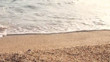 Yakın plan, kumlu sahil boyunca, sörf köpüğü içinde, kadın bacakları yürüyor. Kadın bir seyahat çantası taşıyor. seyahat konsepti. Feminizm. Kadın kendi kendine yetebilirliği. Deniz boyunca beklenmedik maceralar konsepti