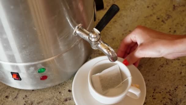 Zbliżenie, żeńska ręka włącza kran gorącej wody, a następnie wlewa wrzącą wodę do filiżanki z torebką herbaty w środku. jadalnia z bufetem lub restauracją all inclusive — Wideo stockowe