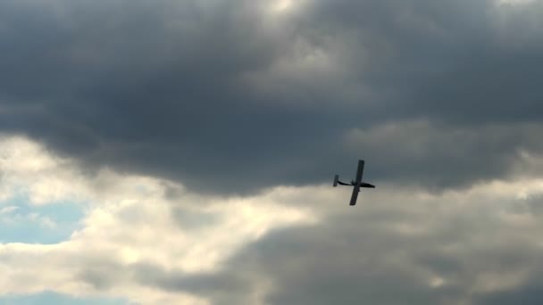 Retro airplane flying against a blue sky with dark storm clouds. sun rays are breaking through the clouds — Stock Video