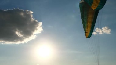 Bir paraglider paraşütünün yakın plan görüntüsü rüzgarda savruluyor, mavi gökyüzü, bulutlar ve güneş