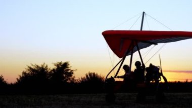 Gün batımında, motorlu planörlerin karanlık silueti yolcu ve pilotla kalkışa hazırlanıyor.