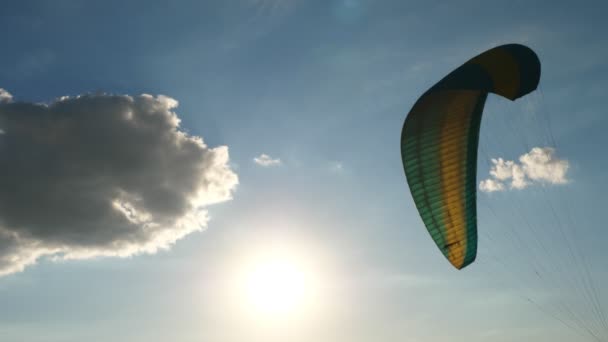 Primer plano de un parapente paracaídas revoloteando en el viento, sobre un fondo de cielo azul, nubes y sol — Vídeos de Stock