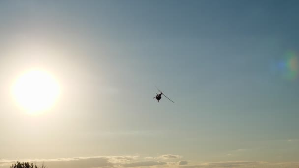 Los contornos oscuros de un helicóptero volando contra un cielo azul y un sol brillante — Vídeos de Stock