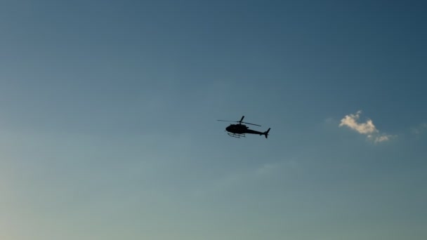 Os contornos escuros de um helicóptero voando contra um céu azul e um sol brilhante — Vídeo de Stock