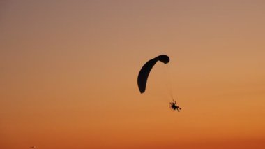 Moto Paraglider 'ın karanlık silueti havada süzülüyor, parlak turuncu bir günbatımının arka planında