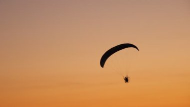 Moto Paraglider 'ın karanlık silueti havada süzülüyor, parlak turuncu bir günbatımının arka planında