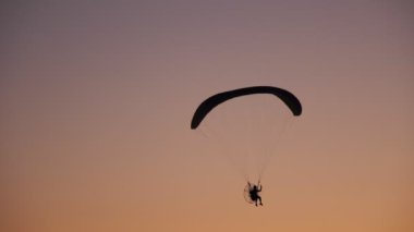 Moto Paraglider 'ın karanlık silueti havada süzülüyor, parlak turuncu bir günbatımının arka planında