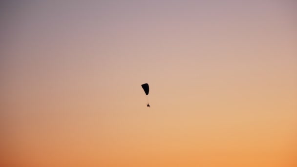 Silueta oscura de Moto Parapente vuela, se eleva en el aire, sobre el fondo de una puesta de sol naranja brillante — Vídeos de Stock