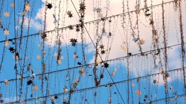 Primo piano, ghirlande di lampadine e stelle argentate, ondeggianti nel vento, luccicanti nei raggi dei soli. Luce decorazione stradale contro il cielo blu. — Video Stock