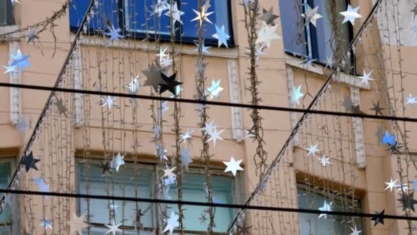 特写，由灯泡和银星组成的花环，在风中摇曳，在太阳光中闪耀。轻型街道装饰 — 图库视频影像